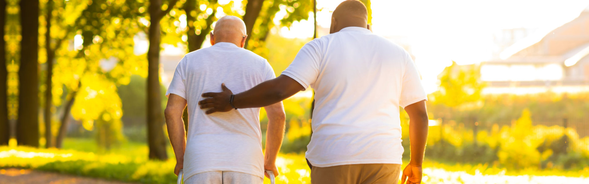 A male assisting a senior man to walk outside